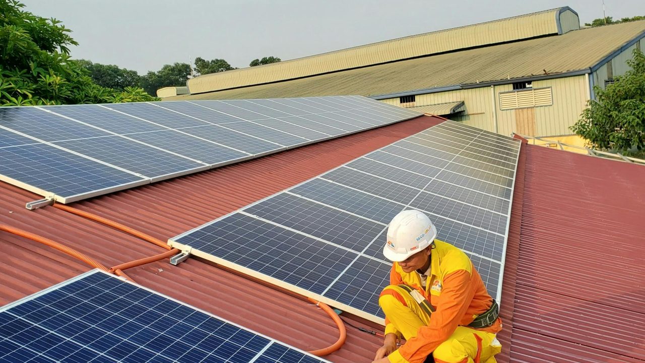 Technician working on solar panel installation on a rooftop under clear sky.
